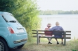 Un couple de seniors assis sur un bans observe le lac lors d'une sortie avec une voiture Citiz bleue.